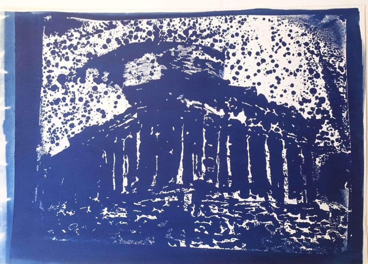 Cyanotype print in deep blue showing a ruined Doric temple with a row of columns and a broken pediment, rendered in heavy blotchy marks, against a white sky densely scattered with round blue spots.