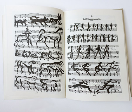 Open sheet music book with black ink silhouettes of animals and human figures in walking and running poses drawn directly over the printed musical staves.