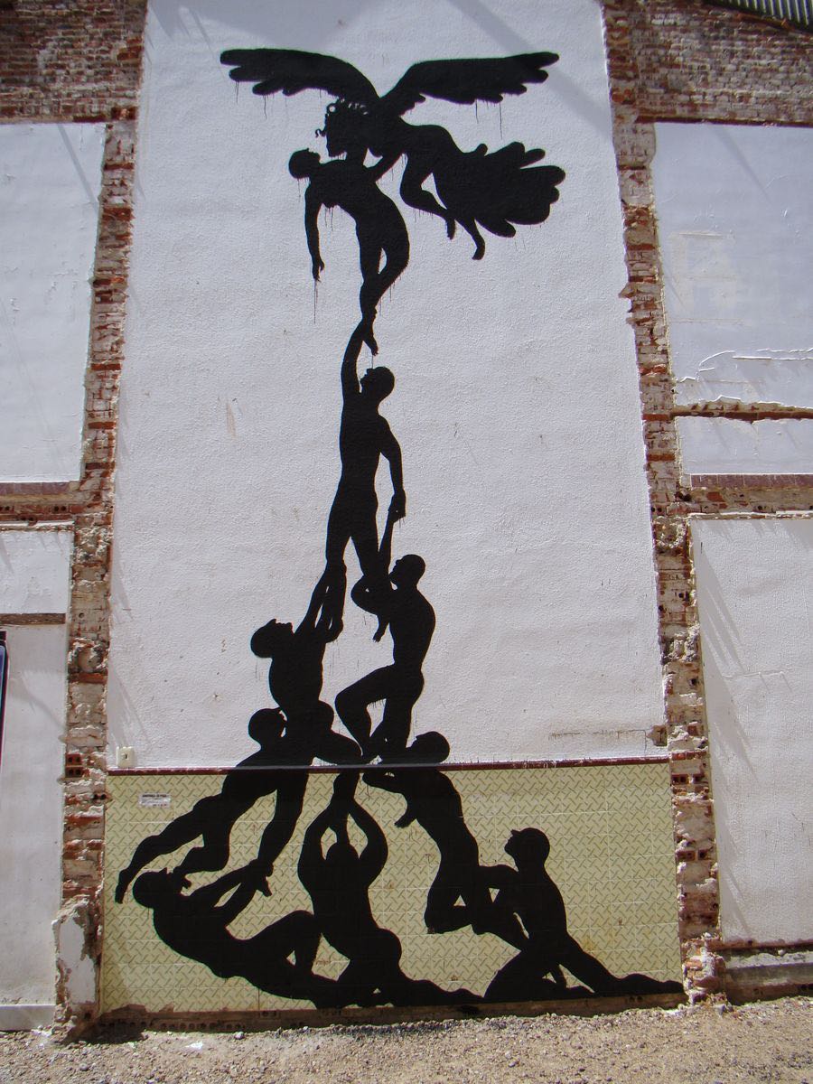 Close-up of black silhouette figures painted directly onto patterned ceramic tiles, overlapping torsos and arms in a tangled embrace, a faded poster fragment visible in the corner.