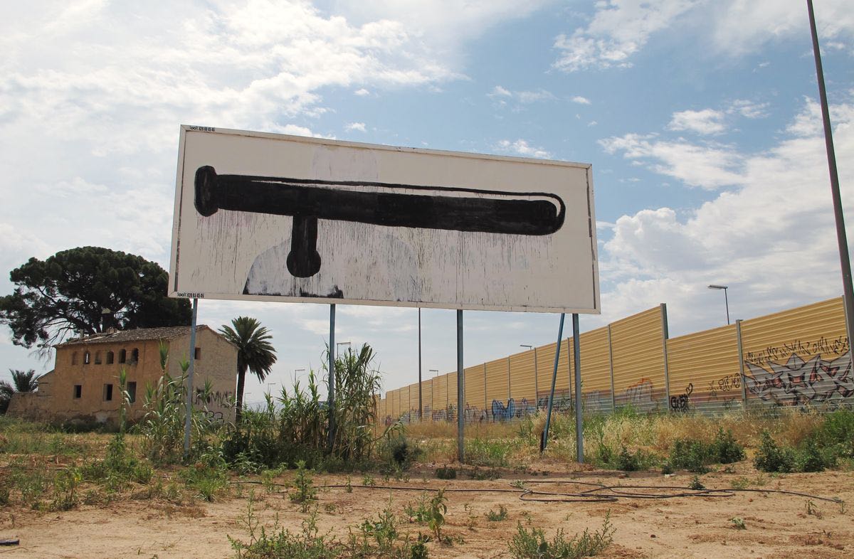 Two roadside billboards side by side, one an advertisement for a clothing shop, the other painted with large black scissors forming a profile face, open grassy field in front.