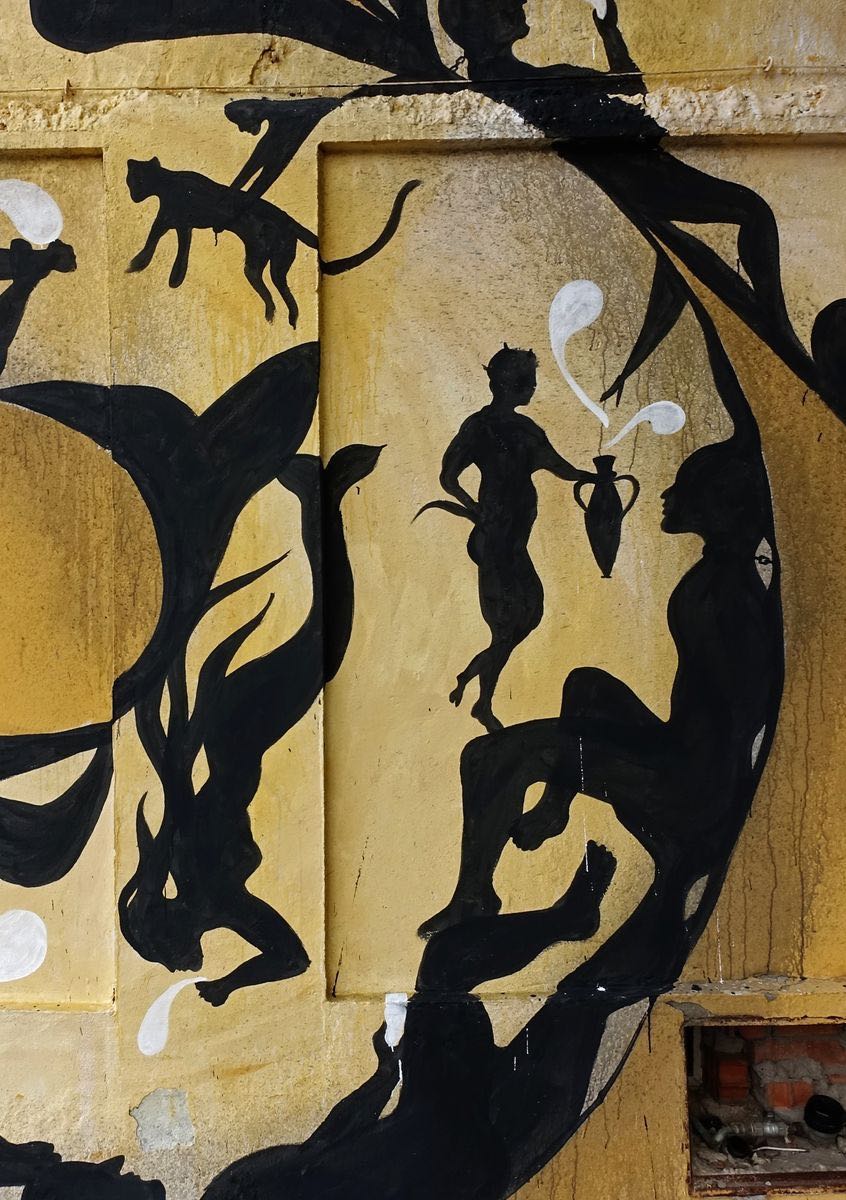 Detail of the snake mural's coiled body filled with black silhouettes of a running cat, a mythological centaur-like figure pouring a jug, and a reclining figure, white splash shapes accenting the yellow background.